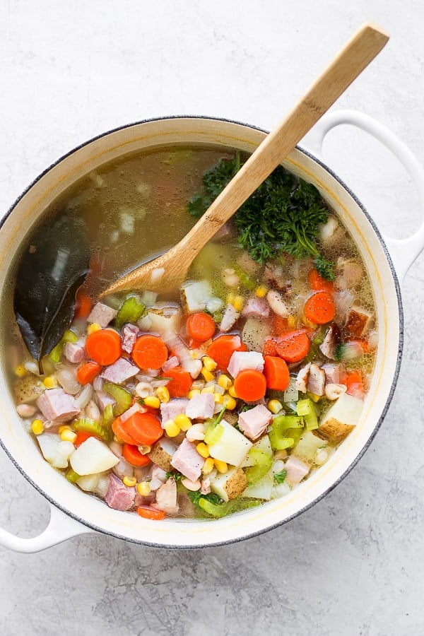 Fully cooked leftover ham bone soup in a white dutch oven.