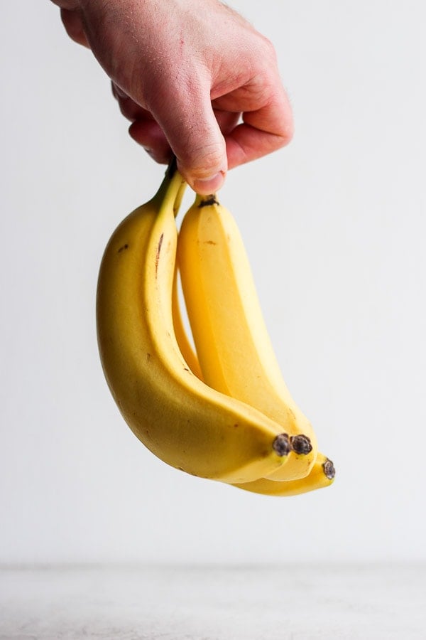 A hand holding three ripe bananas.