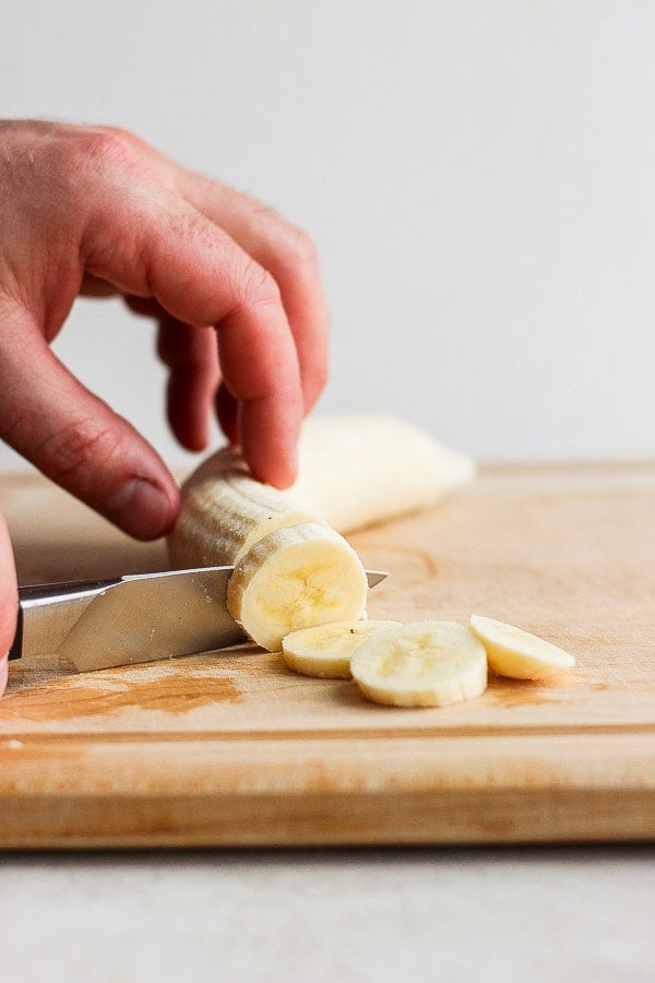 A banana being cut into slices on a cutting board.