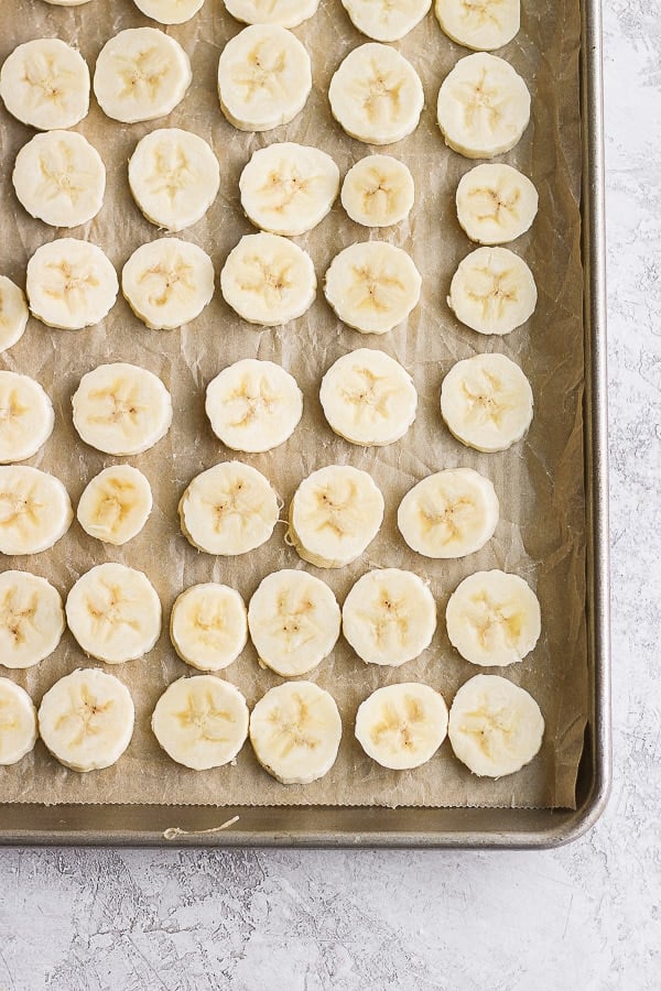 Banana slices in a single layer on a parchment-lined cookie sheet.