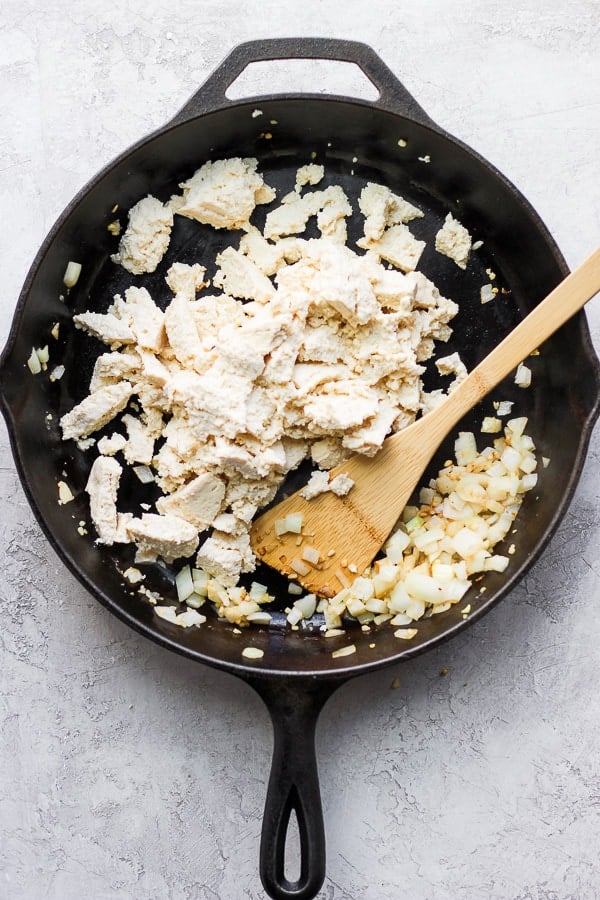 Tofu chunks in a skillet with sautéed onion and garlic.