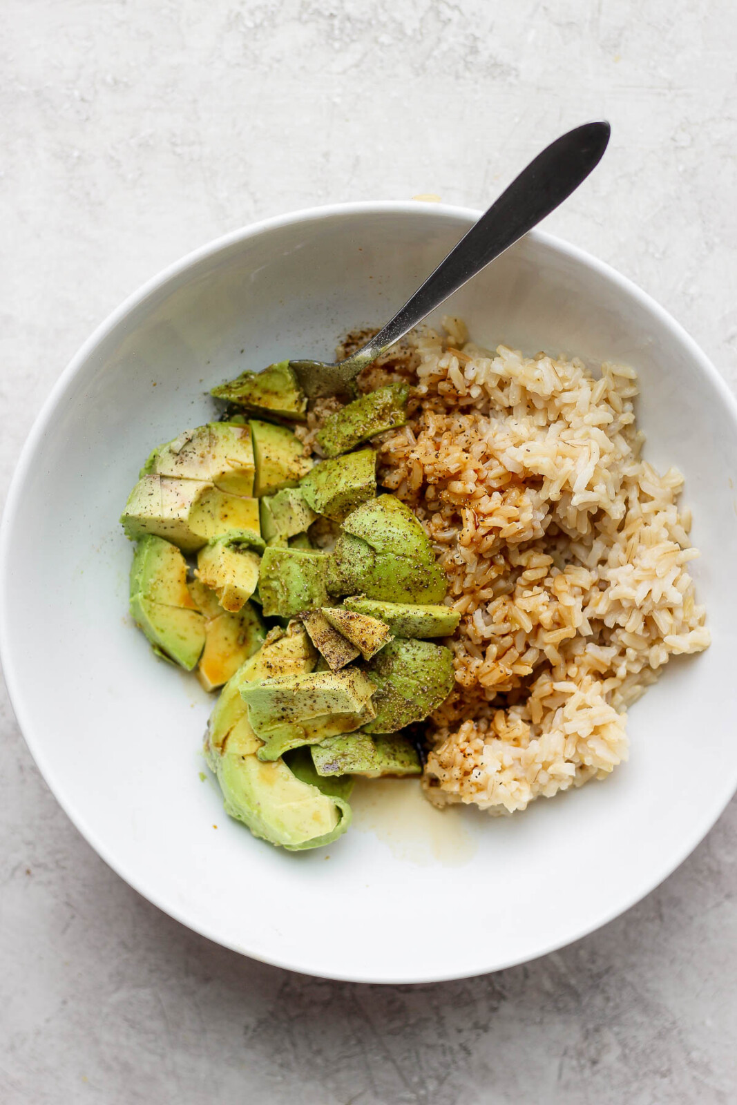 A large white bowl full of avocado, soy sauce, cooked rice and a spoon.
