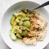 A large white bowl full of avocado, soy sauce, cooked rice and a spoon.