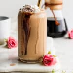 A glass filled with a coffee smoothie on a marble board next to a pink flower.