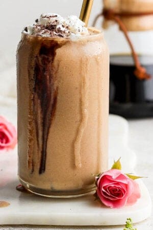A glass filled with a coffee smoothie on a marble board next to a pink flower.
