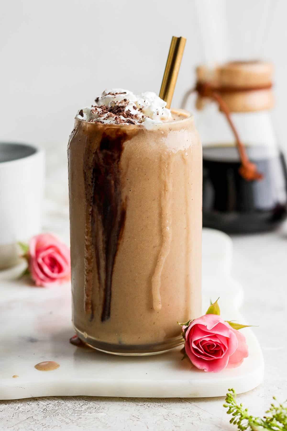 A glass of coffee smoothie with whipped cream and chocolate shavings.