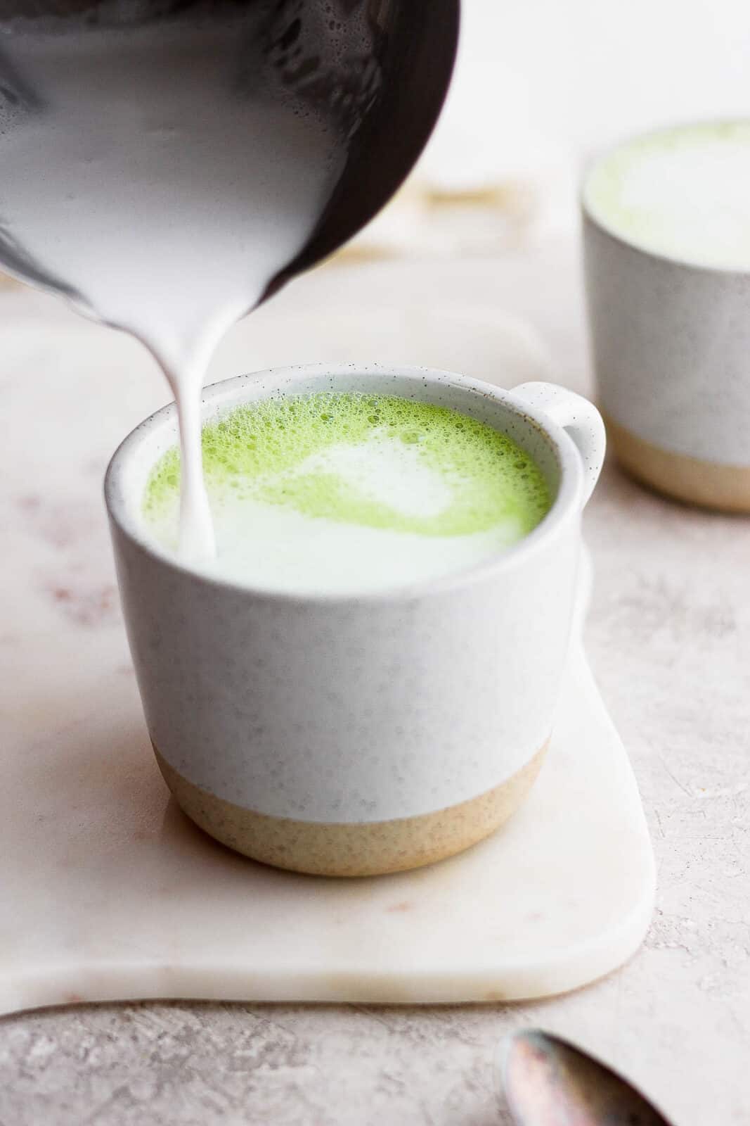 Someone pouring frothed milk on top of the matcha.