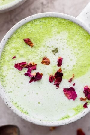 A mug filled with a homemade matcha latte and garnished with dried rose petals.