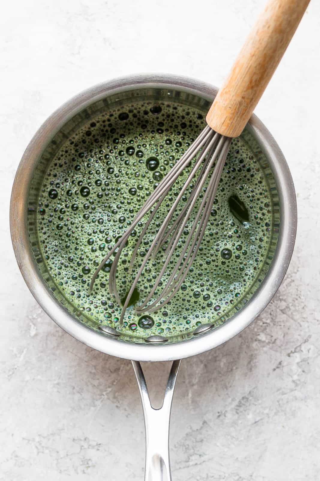Matcha in water in a saucepan with a whisk sticking out of it. 