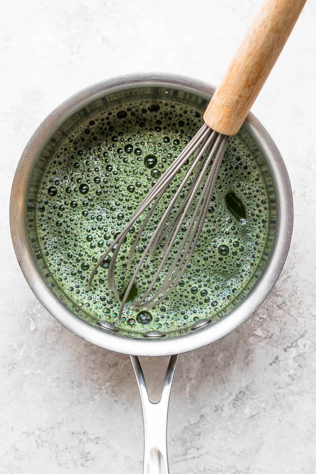 Matcha in water in a saucepan with a whisk sticking out of it.