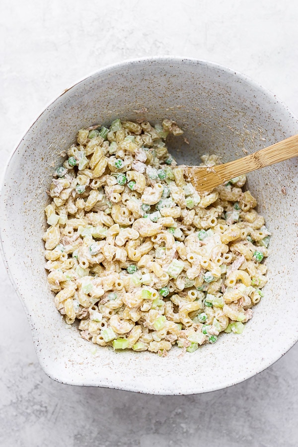A mixing bowl filled with tuna macaroni salad and a wooden spoon sticking out.