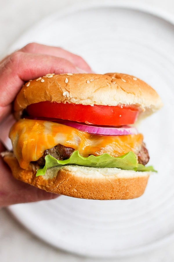 A hand holding a cheeseburger. 