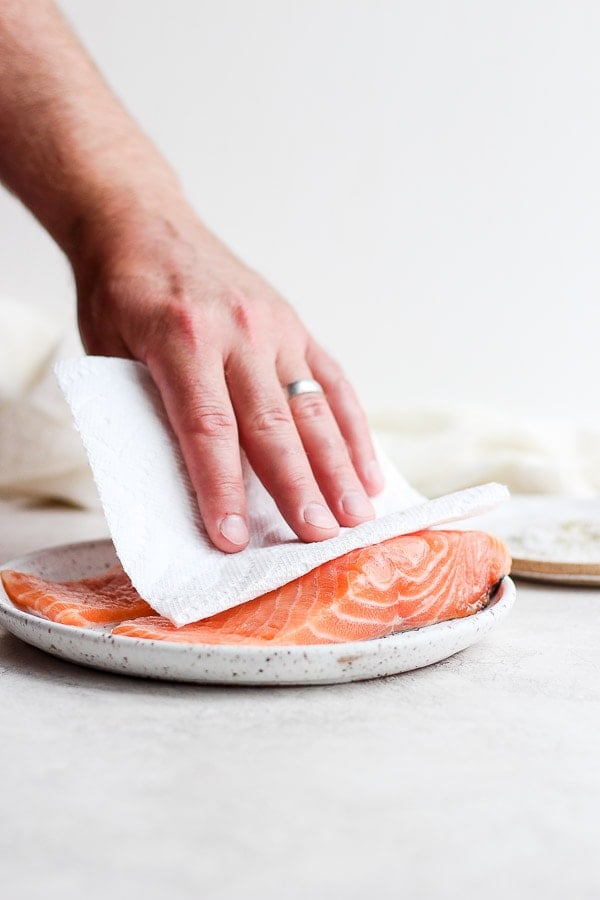 Someone patting dry a piece of raw salmon with a paper towel as they prep it for the grill. 