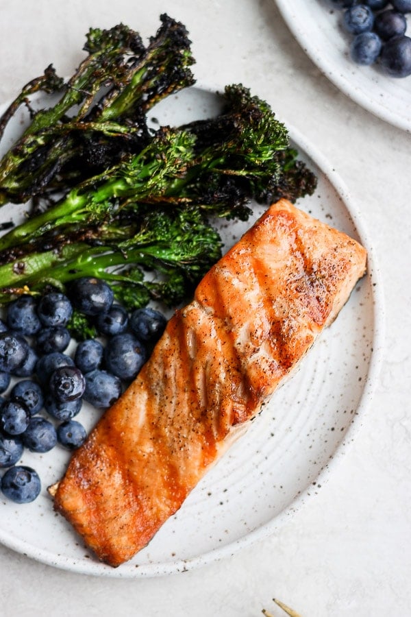 A plate with a grilled salmon filet, grilled broccolini and blueberries. 