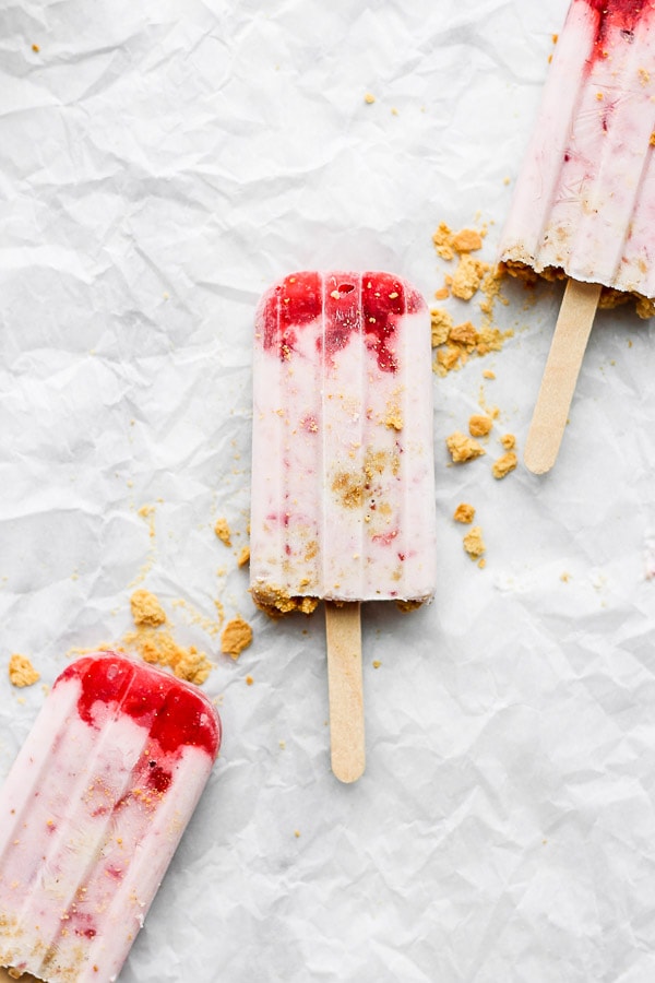 Three frozen strawberry shortcake popsicles on parchment paper.