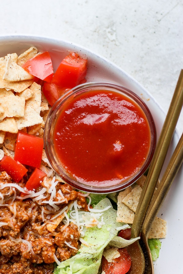 A small dish of taco salad dressing next to a taco salad.