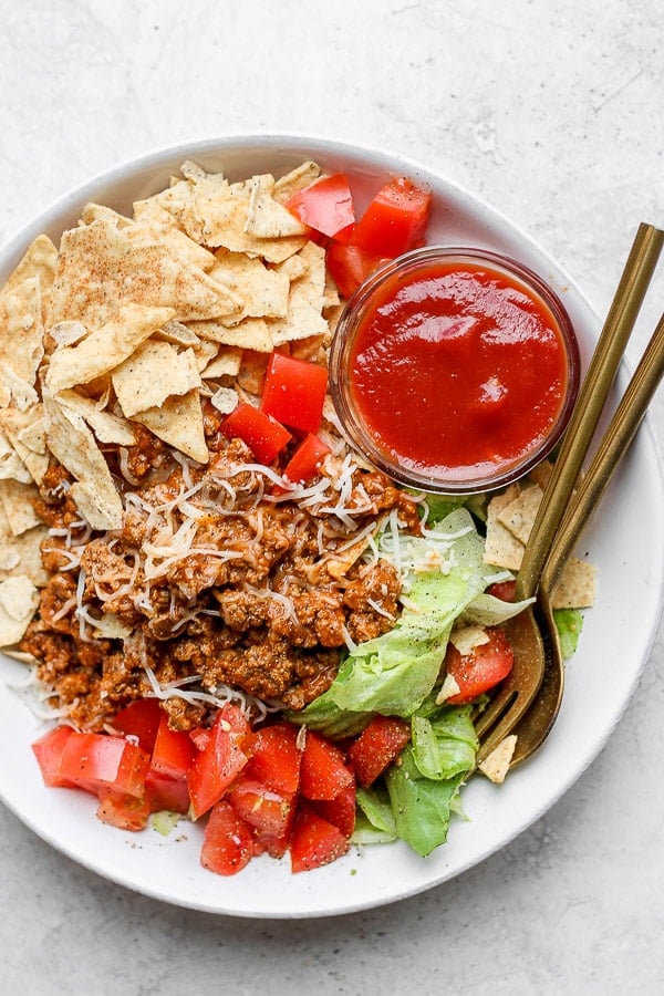 A taco salad with a small clear bowl of taco salad dressing.