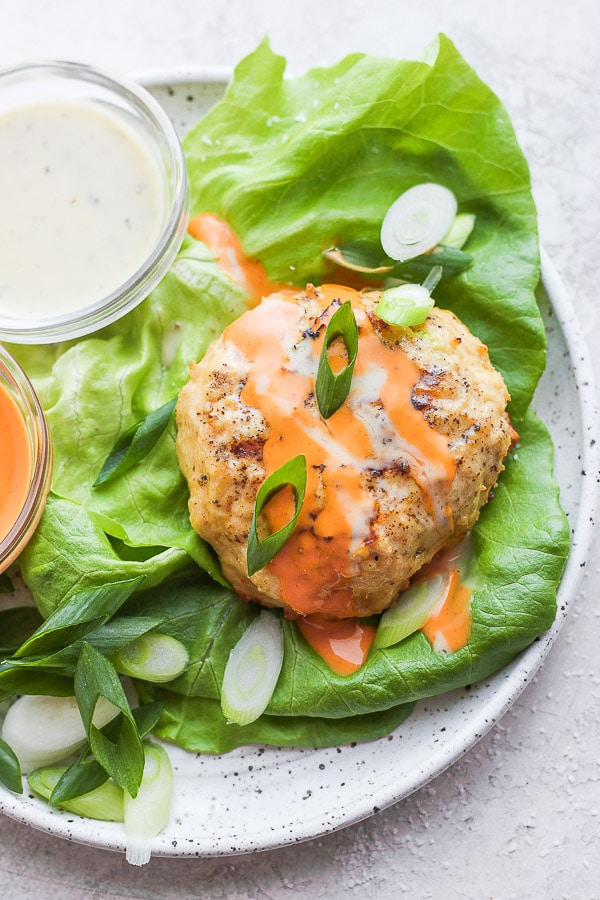 A buffalo chicken burger sitting in a bed of butter lettuce in a shallow bowl.