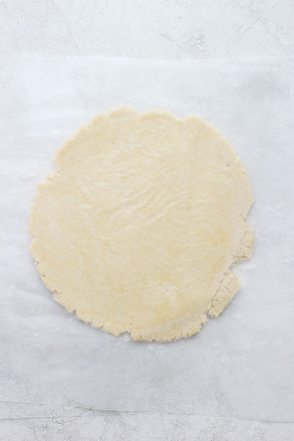 Dough spread in to a circle that's 1/4 inch thick between two pieces of parchment paper.