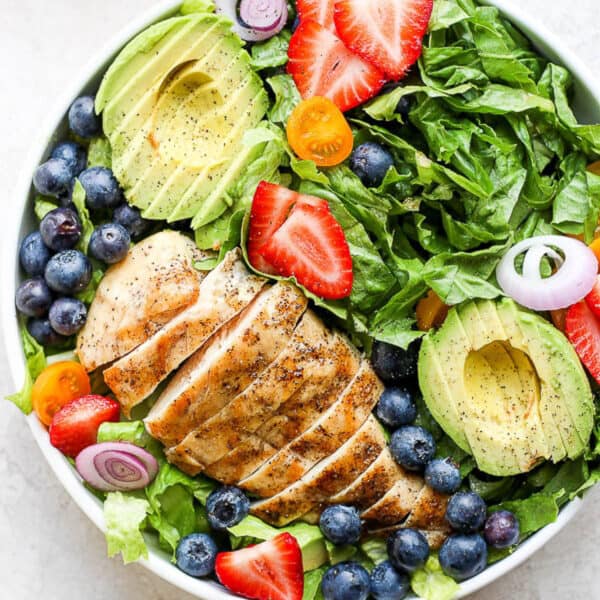 Bowl of grilled chicken salad with avocado, strawberries and blueberries.