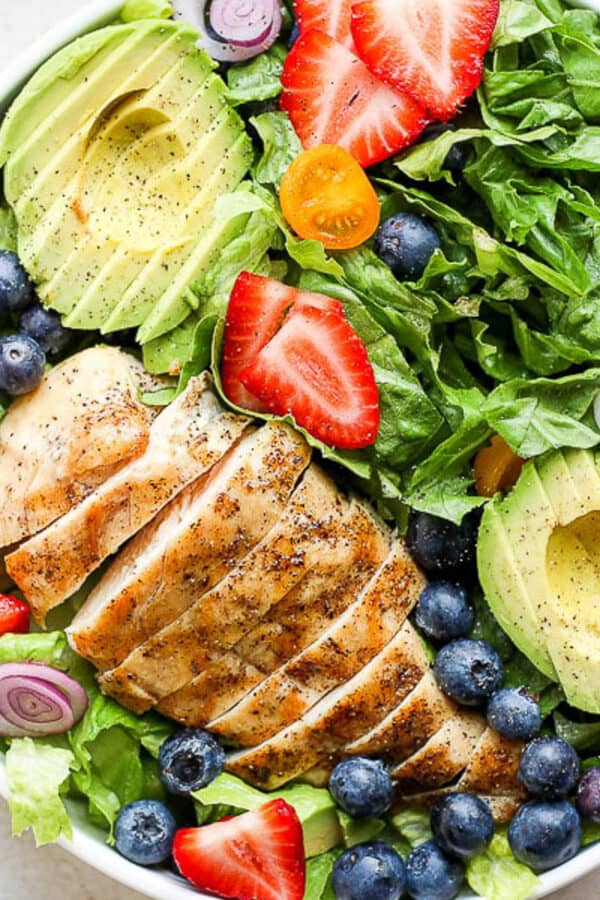 Bowl of grilled chicken salad with avocado, strawberries and blueberries.
