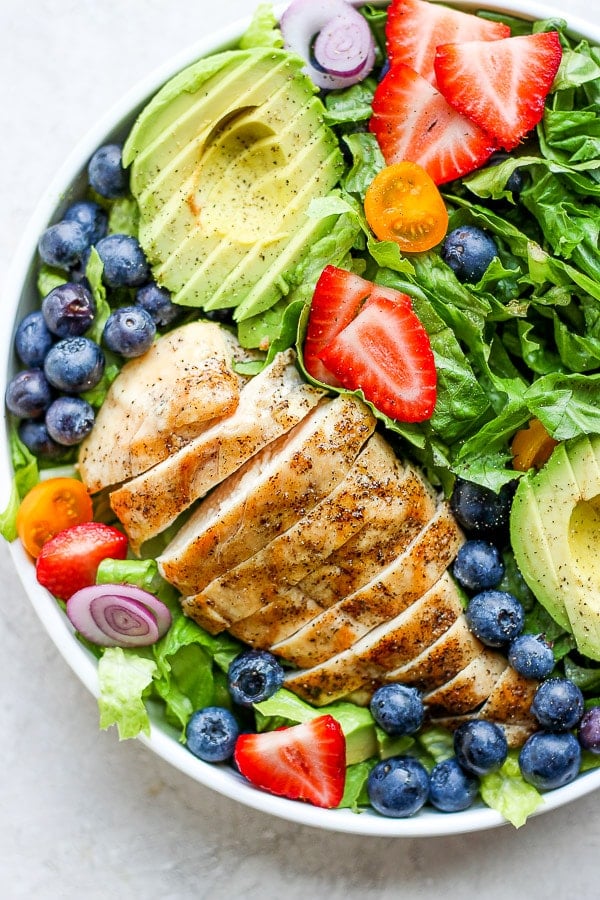 Bowl of grilled chicken salad with avocado and fruit. 