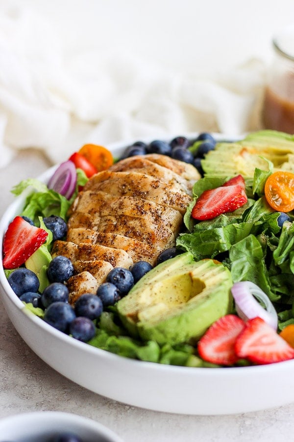 Bowl of grilled chicken salad with avocado and fruit. 