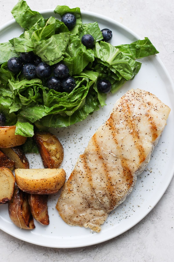 Grilled Red Snapper on a plate with roasted potatoes and salad. 