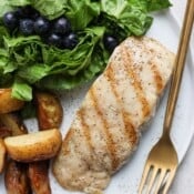A piece of grilled red snapper with a fork, potatoes, and small salad.