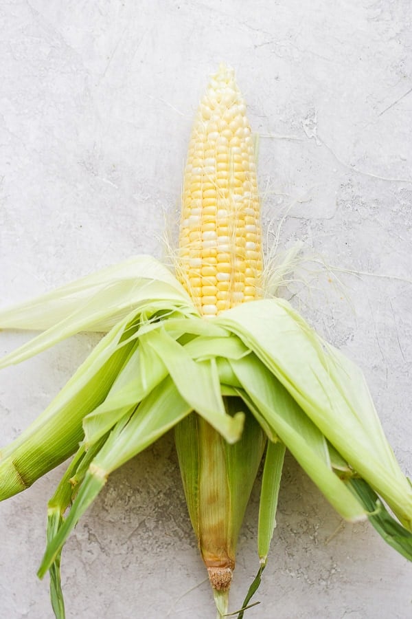 A piece of corn on the cob with the husks pulled back (but not removed). 