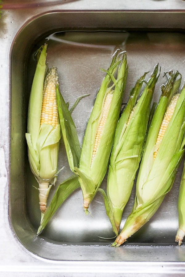 Four pieces of corn on the cob soaking in water. 