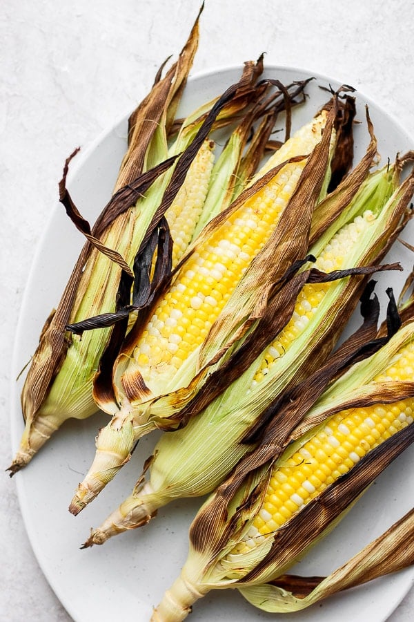 Four grilled corn on the cob with husks on on a platter.