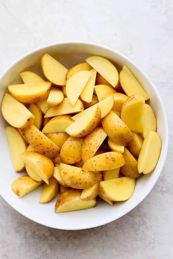 Raw potato wedges in a white bowl.