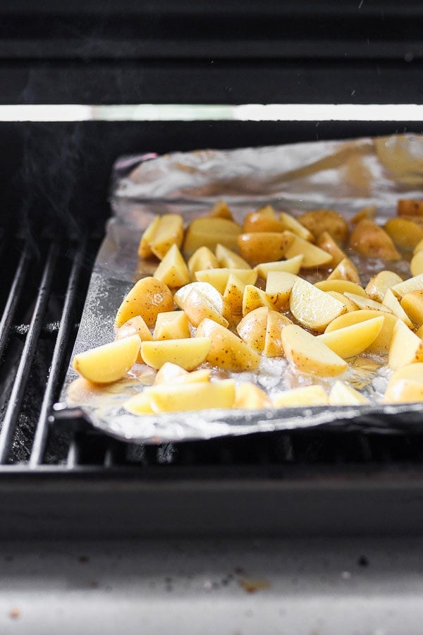 The potato wedges on an aluminum foil sheet on the grill.