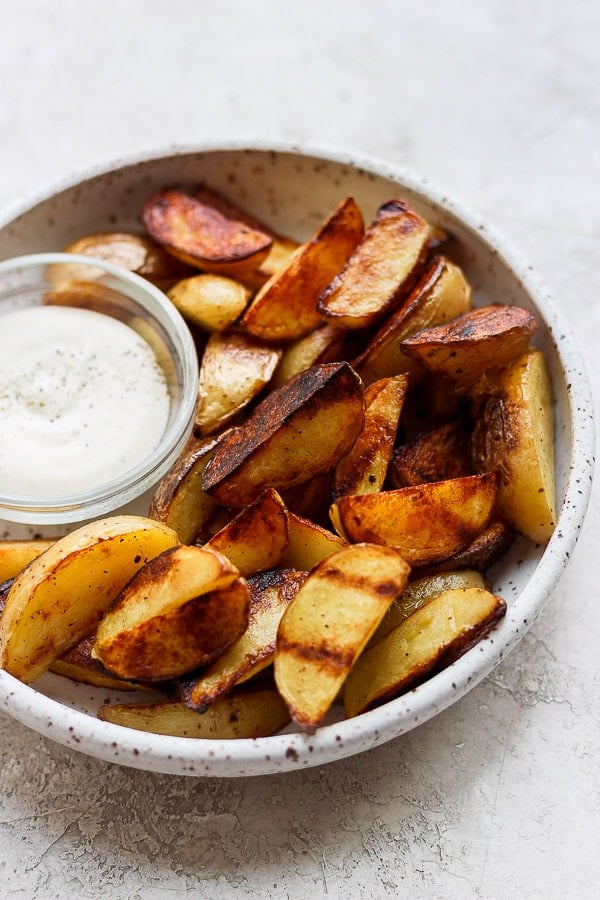 Grilled potato wedges in a dish with a small dish of ranch dressing.