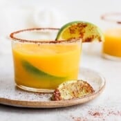 A small mango margarita in a glass, sitting on a plate.