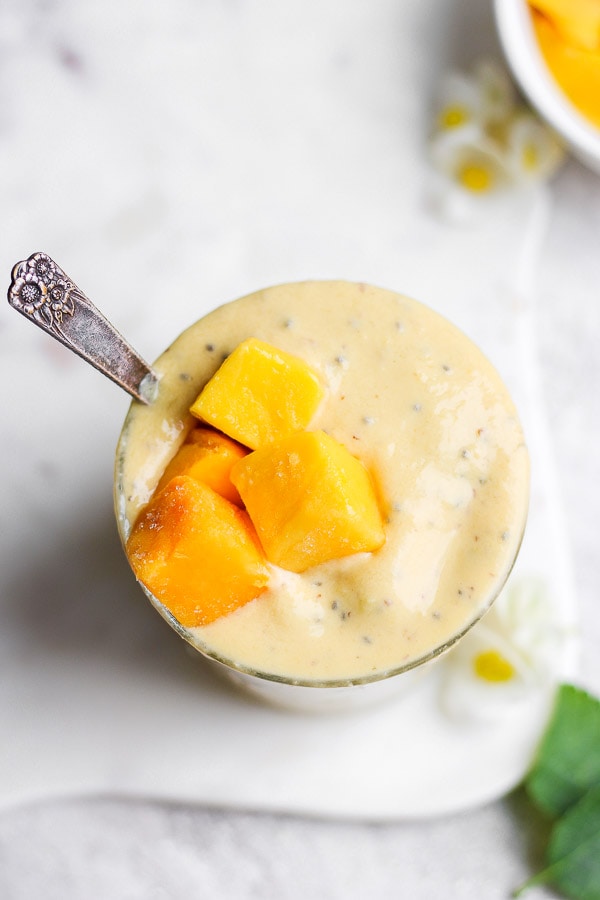 A perfectly blended mango smoothie in a glass with a spoon.