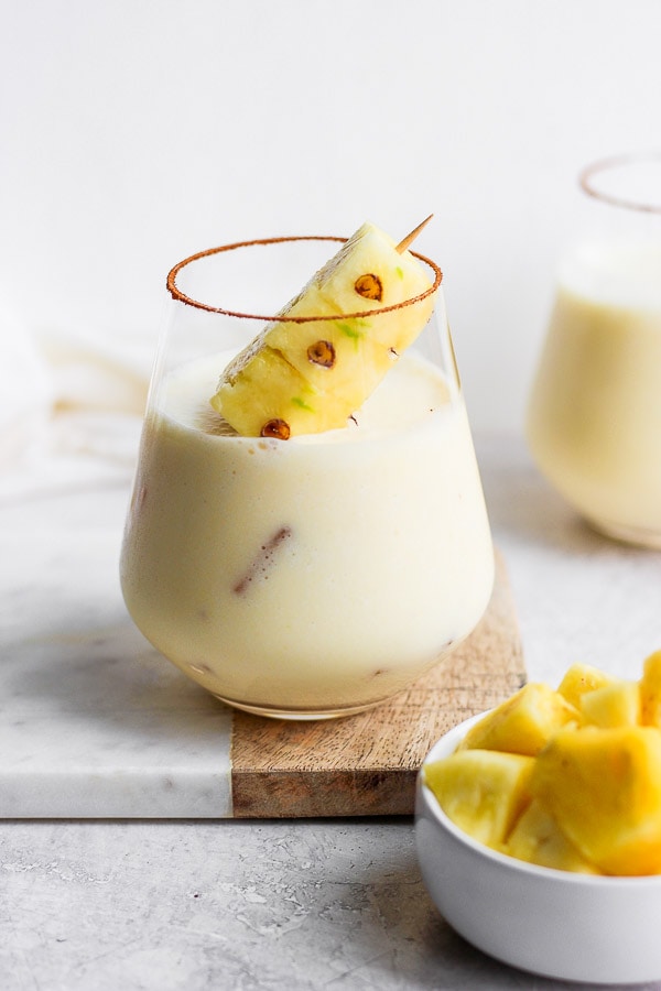 Pina colada in a glass with a cinnamon rim and spear of fresh pineapple.