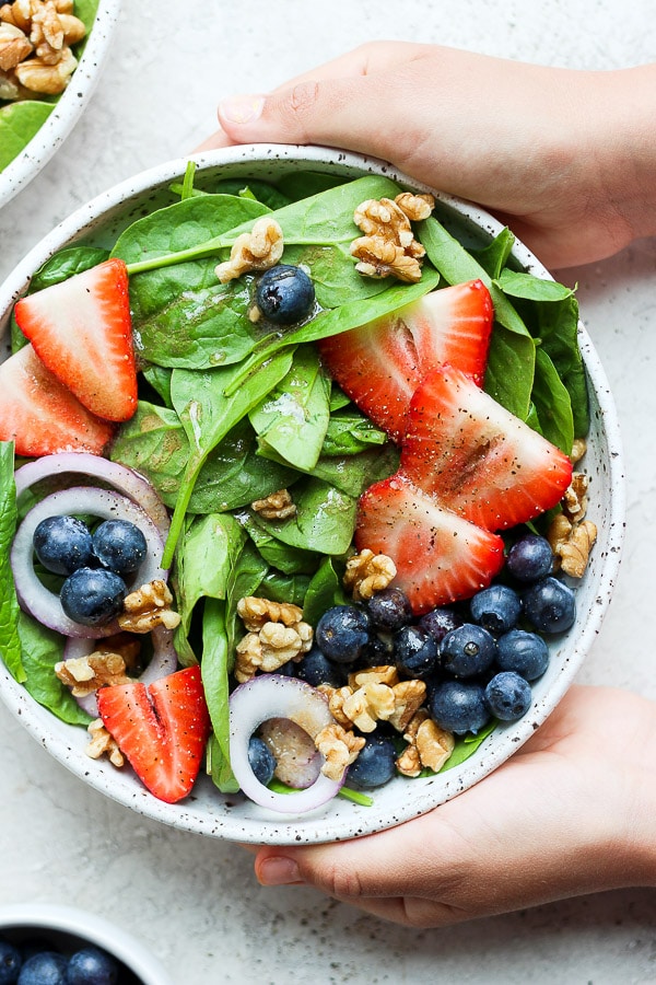 A strawberry spinach salad being held with hands.