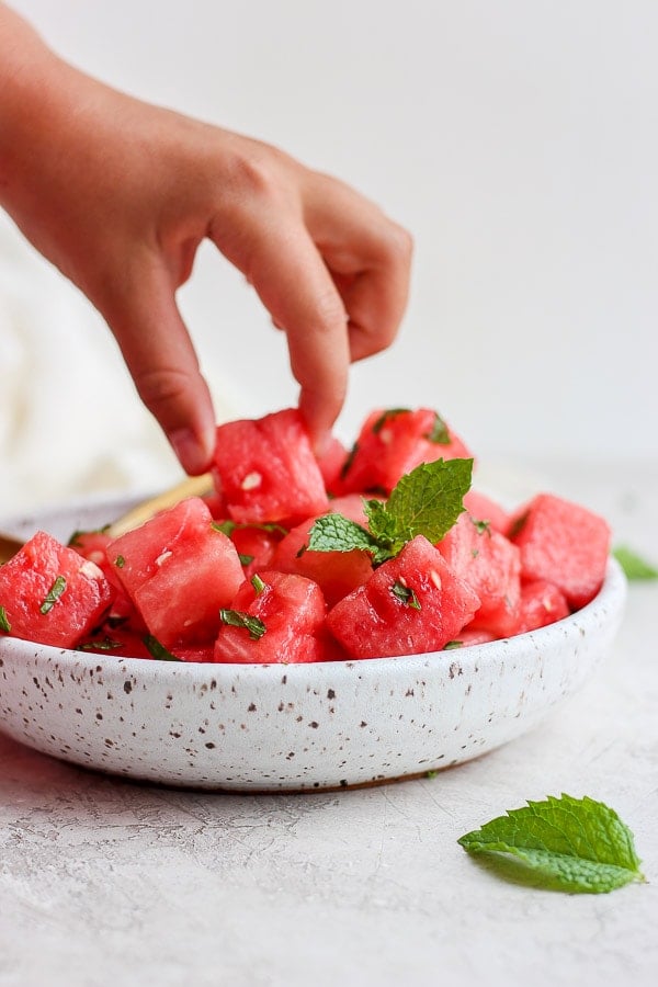 A hand grabbing a piece of watermelon from the plate.