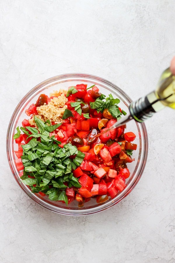 Bruschetta ingredients in a bowl with olive oil being poured in.