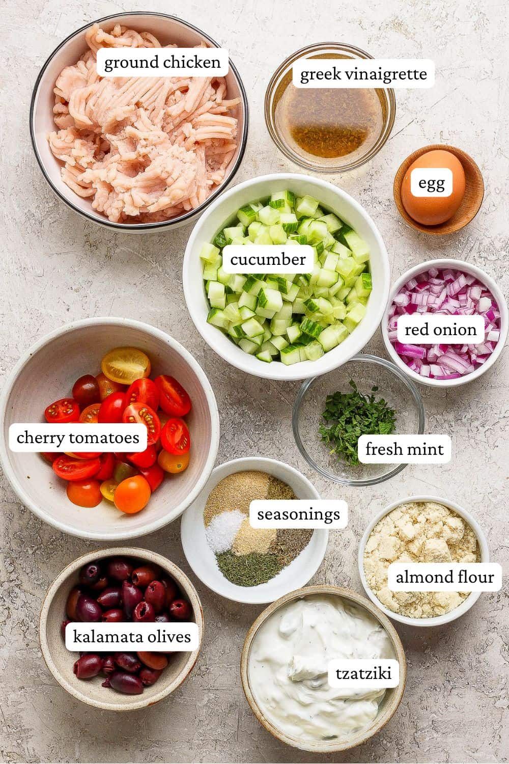 The ingredients for greek chicken meatballs separated out into bowls and labeled.