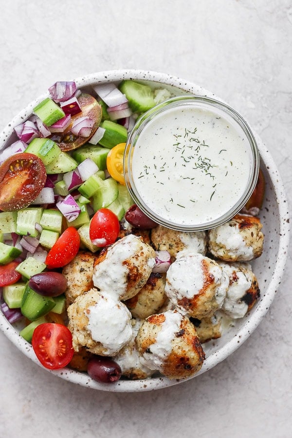 Greek chicken meatballs in a bowl with greek salad and homemade tzatziki sauce. 