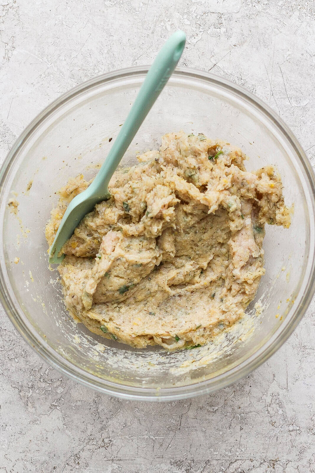 A bowl of combined greek chicken meatball mixture with a spatula sticking out. 
