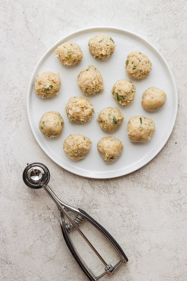 greek chicken meatballs, raw, on a plate with a cookie dough scoop. 