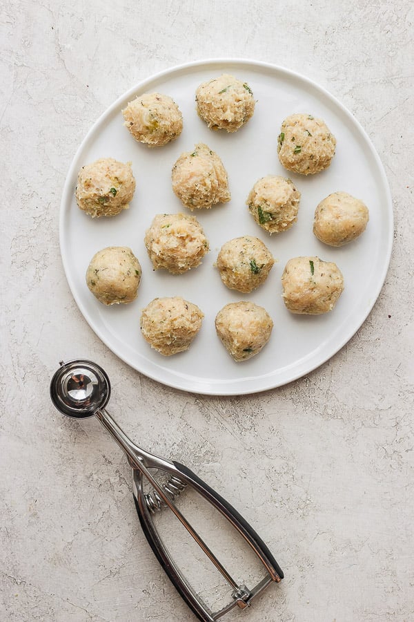 Greek chicken meatballs, raw, on a plate with a cookie dough scoop. 