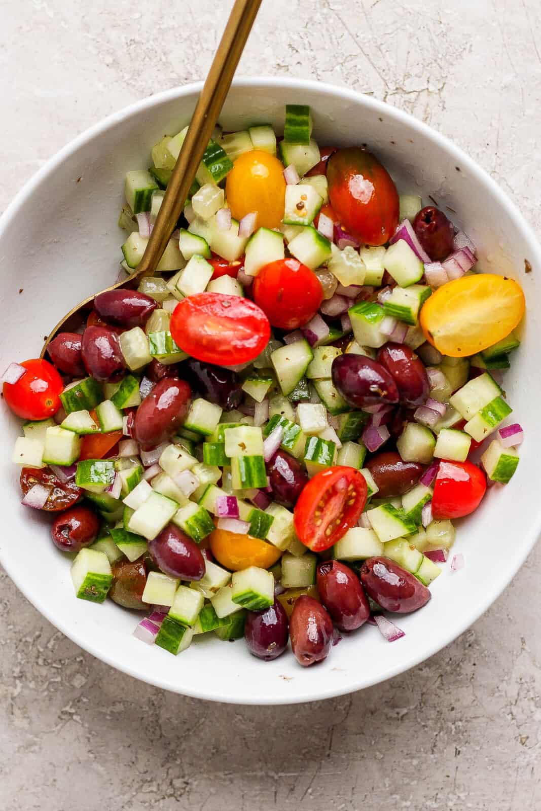 A bowl of prepared Greek salad with a spoon sticking out. 