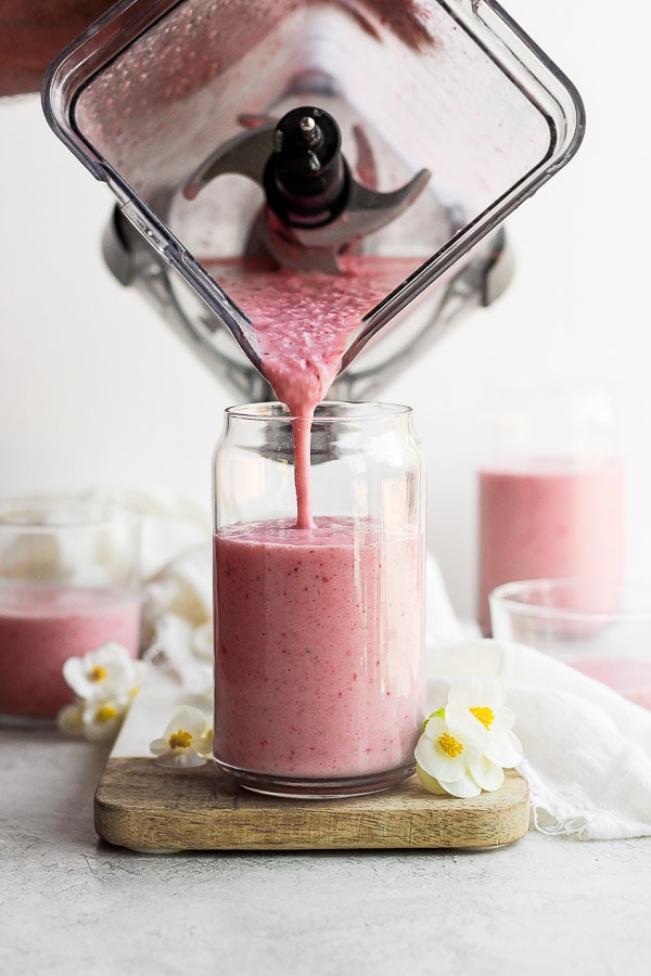 A strawberry smoothie being poured from a blender to a glass.