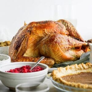 A grilled turkey on a serving platter on a table among various side dishes.