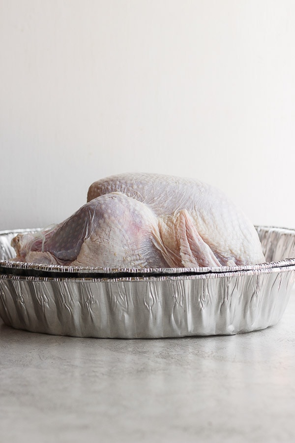 A whole, raw turkey in an aluminum pan. 